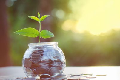 a glass jar filled with coins and a plant growing out of it.